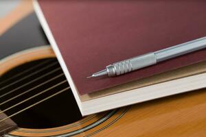 lápiz y cuaderno metido en acústico guitarra. foto