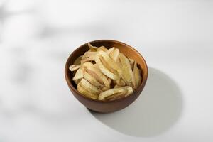 Banana chips in a wooden bowl on a white table photo