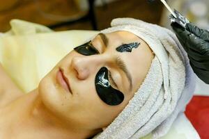 The cosmetologist puts a mask on the face of a young man. photo