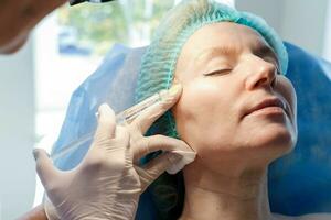 Doctor beautician makes injections in the forehead for patient. photo