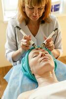 cosmetóloga hace el procedimiento microcorriente terapia en un belleza salón foto