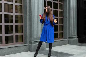 Young woman wearing a blue coat is drinking coffee photo