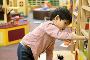 Little Asian boy playing in the interior of a toy wooden house. photo