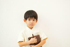 pequeño asiático chico reza participación un cruzar y un religioso libro, cristiano concepto foto