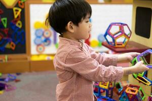 A little Asian boy is playing with a square magnetic puzzle. photo