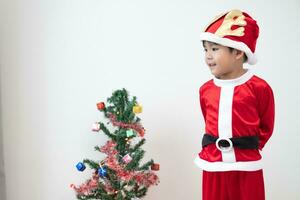 Asian boy wearing Santa costume Standing and playing near A fun Christmas tree on white background. photo