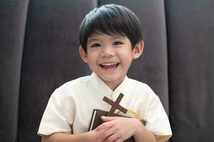 Little Asian boy prays holding a cross and a religious book, Christian concept photo