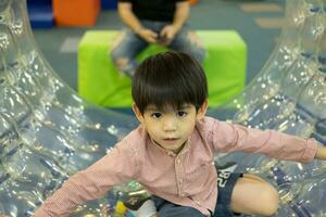 A little Asian boy is playing with a giant, rolling ball with holes. photo