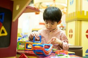 un pequeño asiático chico es jugando con un cuadrado magnético rompecabezas. foto