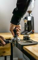 Coffee tamper, a tiny tool that is used to pack or tamp espresso grounds into the basket of espresso machine. Barista tamping coffee grounds into portafilter photo