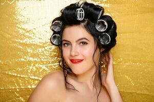 Beautiful girl in hair curlers isolated on gold photo