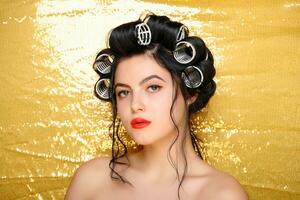 Beautiful girl in hair curlers isolated on gold photo