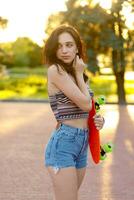 Girl holding a orange skate with green wheels. photo