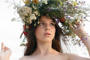 beautiful woman with a wreath on her head sitting in a field in flowers photo