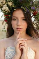 beautiful woman with a wreath on her head sitting in a field in flowers photo