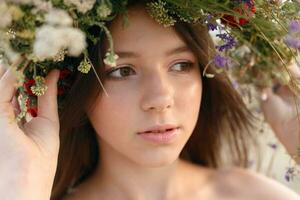 hermosa mujer con un guirnalda en su cabeza sentado en un campo en flores foto