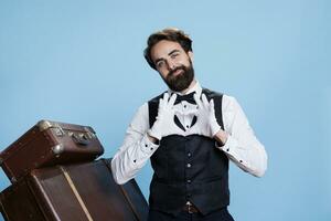 Hotel porter doing heart shape sign in studio and displaying romantic emotions, professional tourism occupation. Young man being sweet and presenting love romance symbol on camera. photo