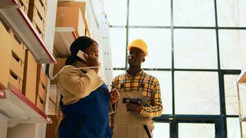 Team of people planning cargo shipment in warehouse, woman answering phone call in depot. Male employee checking list of products while manager talks on landline phone. Handheld shot. photo