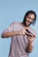 Arab man with carefree expression playing mobile game application on smartphone. Happy smiling young gamer enjoying entertainment technology while using telephone application photo