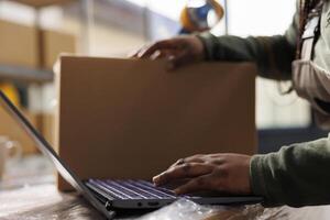 Storage room employee checking merchandise checklist on laptop computer before start working at customers orders in warehouse. Stockroom supervisor preparing packages for delivey. Close up photo