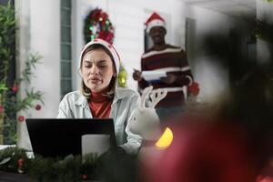 Employee working on company project with deadline approaching soon before winter holiday season. Worker solving tasks and finishing paperwork in festive decorated office during Christmas photo