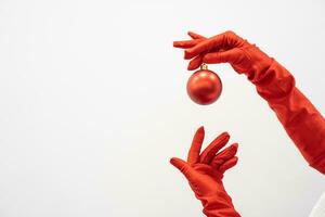 The hands of woman in elegant red dress and gloves hold bright Christmas ball, ready to add shine to any Christmas composition. Winter holidays and atmosphere new year and preparations for Christmas. photo