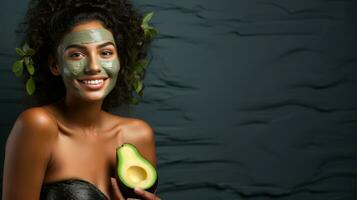 Beautiful african american woman with facial mask and avocado on green emerald background. photo