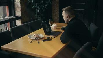 a elegante homem comunica com uma mulher através da vídeo chamar. uma homem é sentado dentro uma moderno cafeteria e usando uma computador portátil para uma vídeo chamar. video