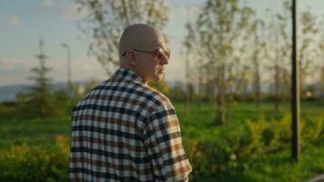 A stylish, satisfied and confident bald middleaged man walks through a city park. A walk on a warm summer evening adds tone and positivity. video