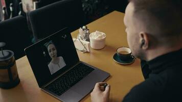 A man in a dark sweater sits in a cafe with a laptop and video chats with a woman. A video call allows you to communicate more effectively.