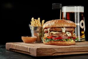 Burger with two patties, blue cheese, caramelized onions, tomatoes and arugula served with amber lager, fries and sauce photo