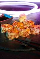 Closeup of uramaki rolls with melted cheese and bonito flakes on slate board with bright LED strip photo