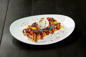 Belgian waffle with chocolate and caramel toppings, biscuits, dragee candies and ice cream photo