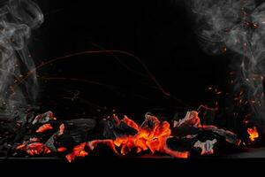 Hot burning coals on barbecue tray on black background with sparks and white smoke photo