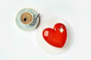 Heart shaped mousse cake in red icing with cup of espresso photo