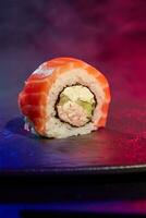 Closeup of one Philadelphia sushi roll with salmon on bright multicolored background of neon lighting photo