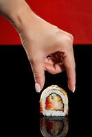 Female hand reaching out to roll with shrimp, tobiko, cucumber, eel and sesame photo