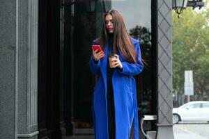 Young woman wearing a blue coat is drinking coffee photo