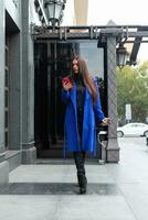 Young woman wearing a blue coat is drinking coffee photo