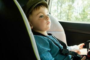 Toddler boy sitting in child safety seat in car. Car traveling with kid. photo