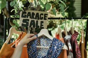 Garage sale. Female hands picking out used apparel hanging on rack. photo