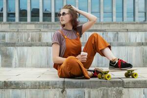 Skater young woman resting drinking coffee after skateboarding. photo