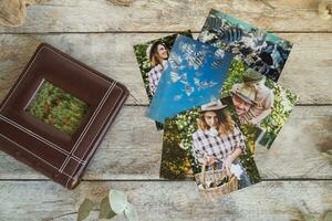 Printed photos and photo album on wooden board. Top view.