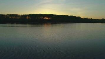 Basso angolo volante per il sinistra al di sopra di il lago contro il sole a tramonto. il sole brilla attraverso il alberi. video