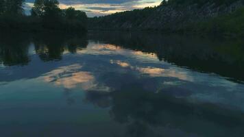 Low angle fast fly over the river at sunset. Rocks with green trees on a riverside. Colorful sky with clouds. video