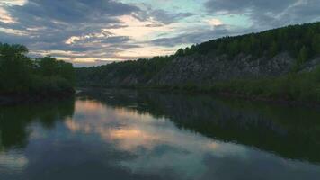 schnell fliegend nach vorne und nach oben Über das Fluss zu Felsen mit Grün Bäume beim Sonnenuntergang. video