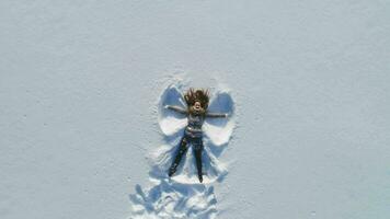 Young cheerful woman is lying on snow and is making snow angels. Slow motion. Aerial view with rotation. video