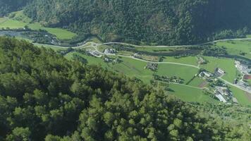 fliegend Über Berg Steigung mit Grün Bäume und Dorf im Norwegen beim sonnig Sommer- Tag. Antenne verraten Schuss. Drohne ist fliegend rückwärts, Kamera ist kippen oben video