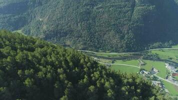 Flying over Mountain Slope with Green Trees and Village in Norway at Sunny Summer Day. Aerial View. Drone is Flying Forward, Camera is Tilting Down video