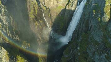 voringfossen vattenfall, klippor och regnbåge i Norge på solig sommar dag. antenn se. Drönare flugor bakåt video